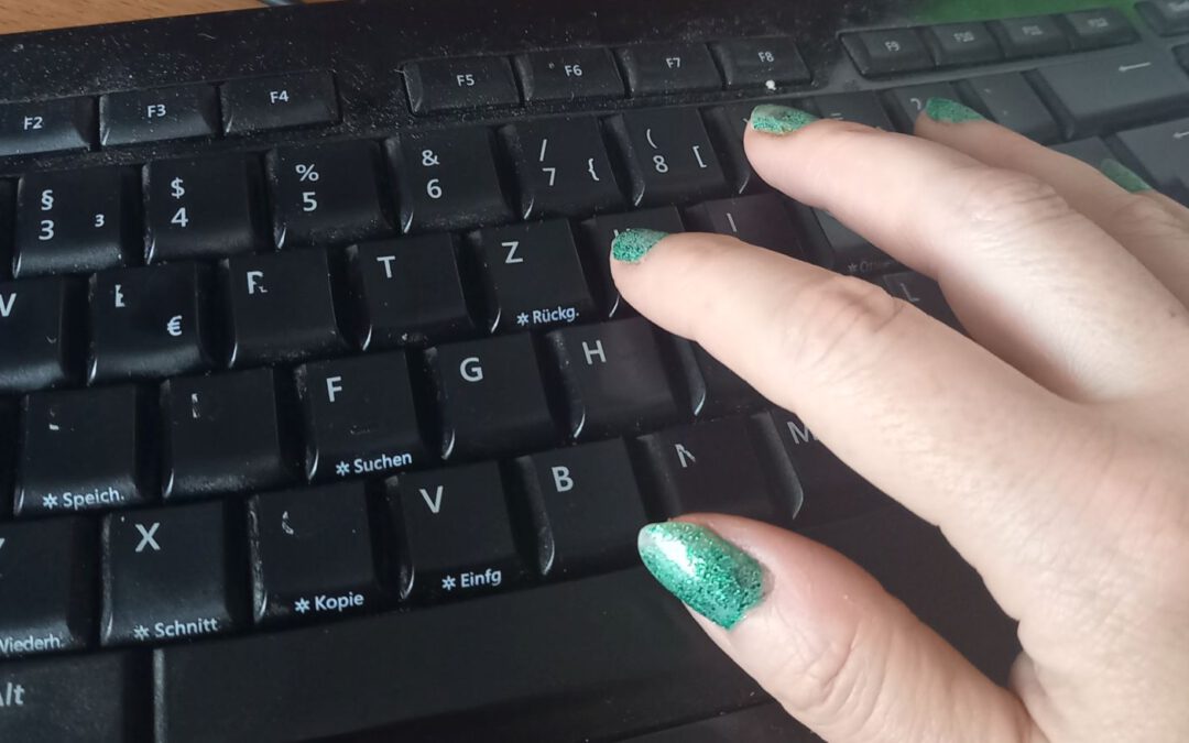 Hand mit grünen Nägeln auf schwarzer Computertastatur
