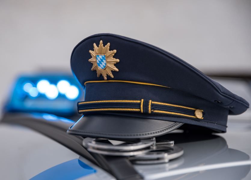 Polizei-Dienstmütze auf Autodach von Polizeiauto. Blaulicht leuchtend daneben