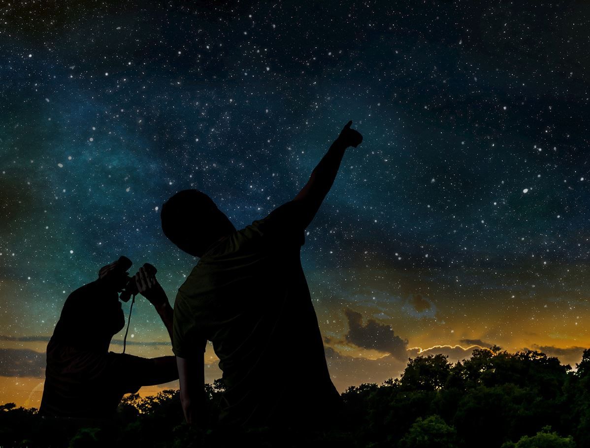 Zwei Männer schauen in den Himmel hinauf. Dunkle Stimmung. Am Himmel lauter Sterne. Einer der Männer hält ein Fernglas.