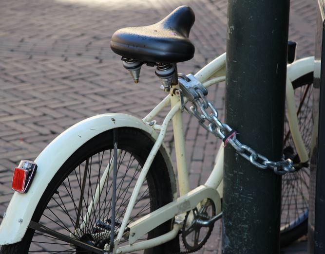 Weißes Fahrrad mit Eisenkette gesichert an einen Masten gelehnt