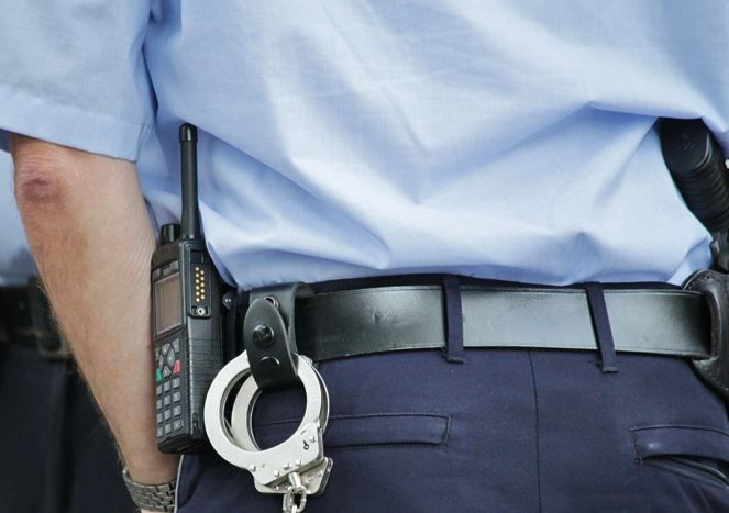 Polizist von hinten mit Handschellen am Gürtel und Handy