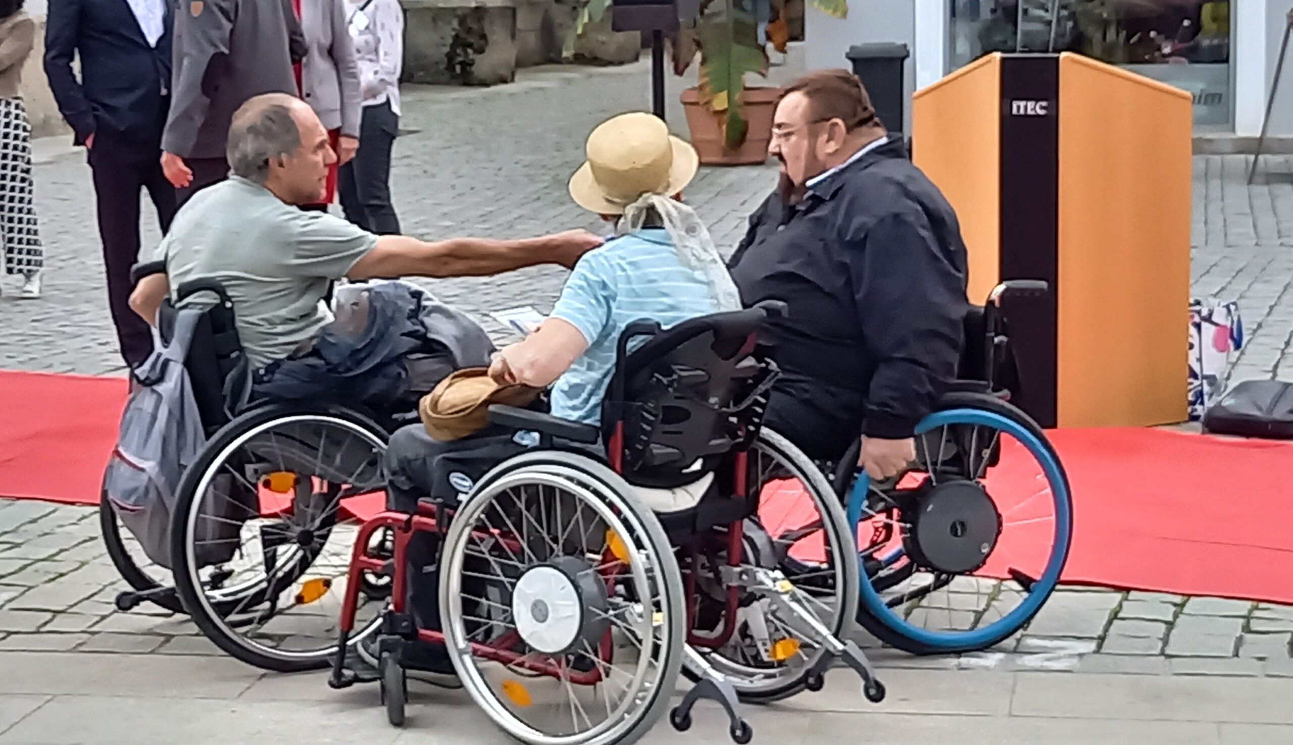 2 Rollstuhlfahrer und eine Rollstuhlfahrerin unterhalten sich beim roten Teppich