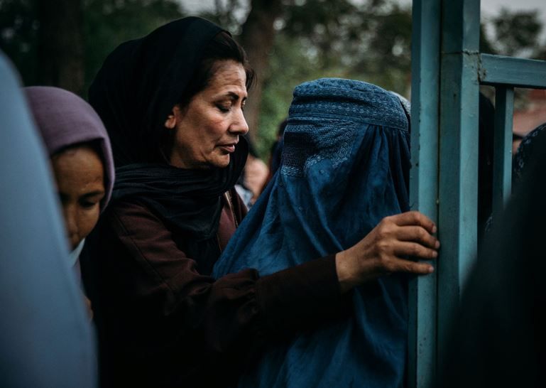 Eine Frau mit Burka und zwei weitere Frauen mit Kopftuch öffnen Türe