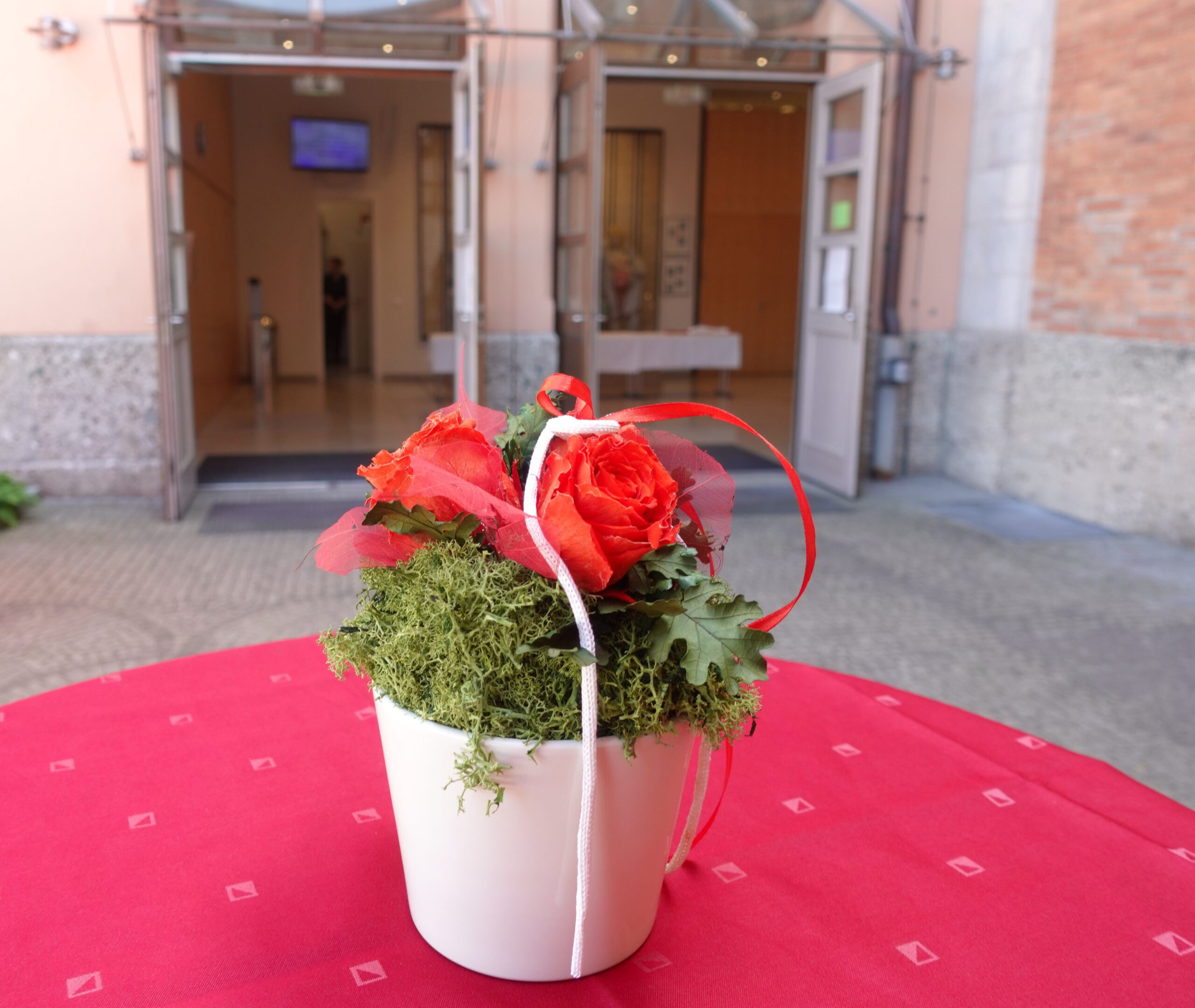 Blick über kleinen weissen Blumentopf mit Rosen hin zu den Eingangstüren des Rosenheimer Rathauses