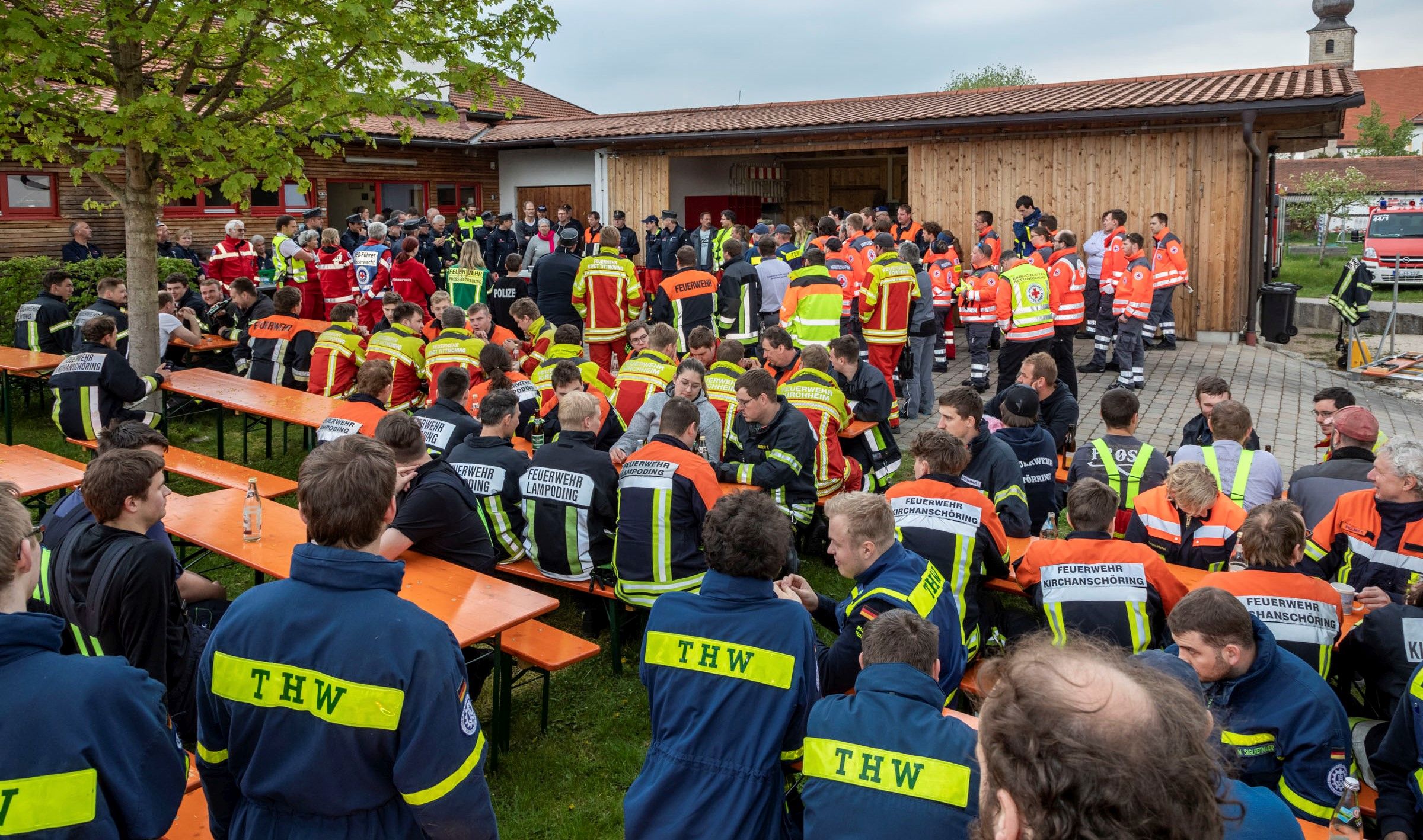 Rund 100 Feuerwehrler sitzen auf Wiese bei Besprechung