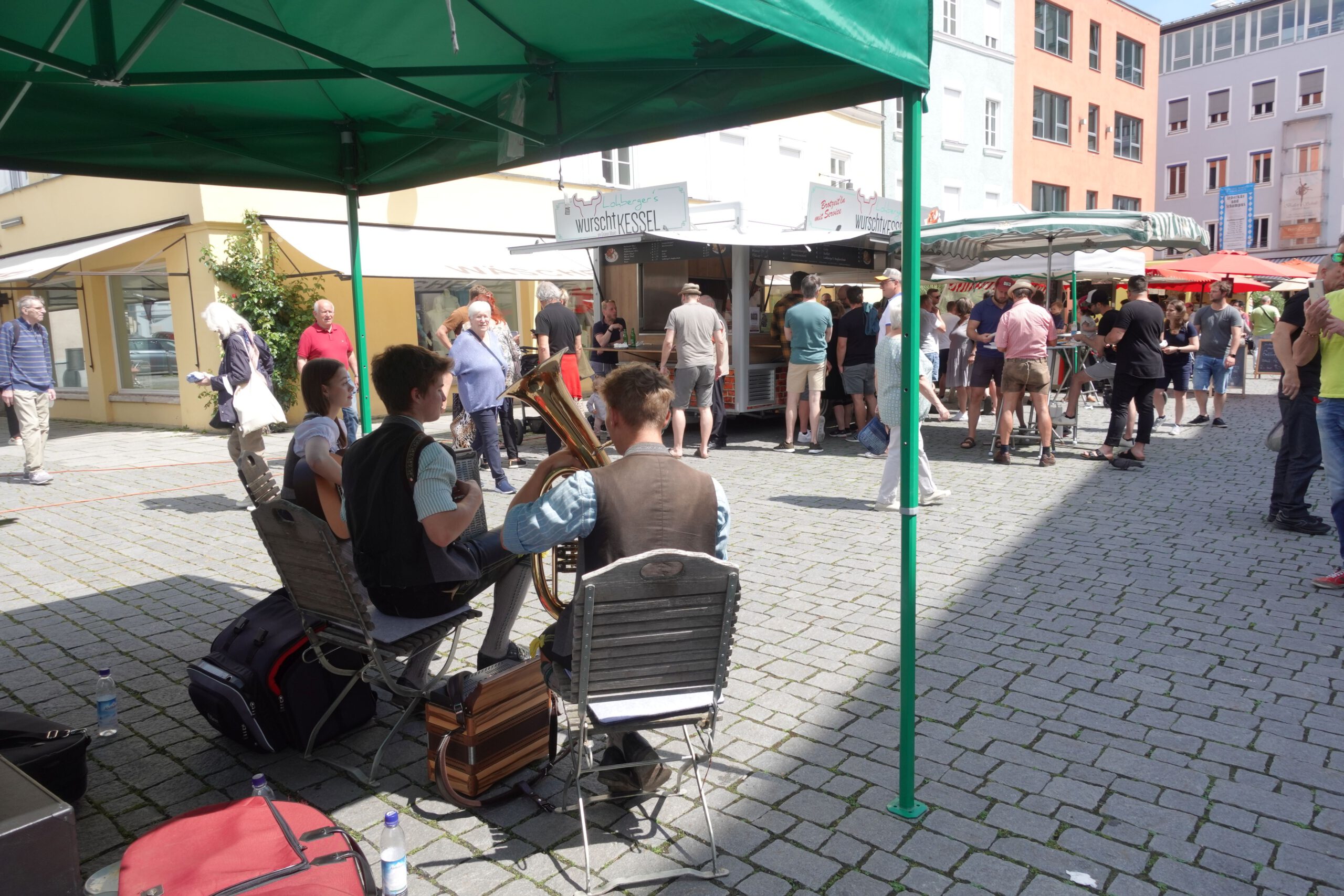 Blick auf den Gruenen Markt in Rosenheim. Musiker spielen im Vordergrund. Blick über sie hinweg auf das Markttreiben