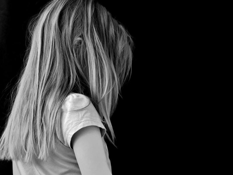 schwarz-weiss-Aufnahme: Mädchen mit T-Shirt, lange Haare, Gesicht erkennt man nicht, lässt Kopf traurig hängen