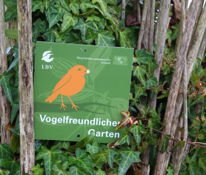 Die grüne Plakette mit orangem Vogel an Zaun