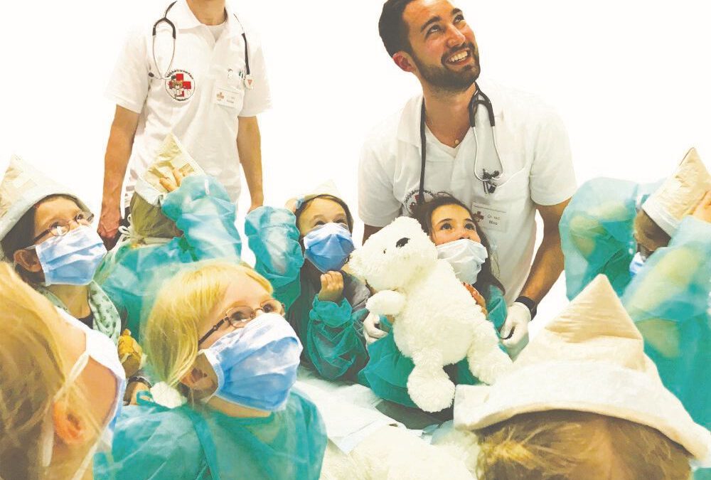 Zwei junge Ärzte mit vielen Kindern und Kuscheltieren um sich herum