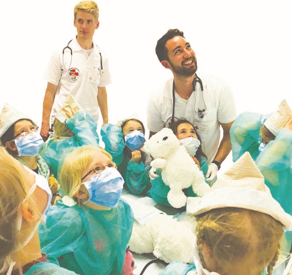 Zwei junge Ärzte mit vielen Kindern und Kuscheltieren um sich herum