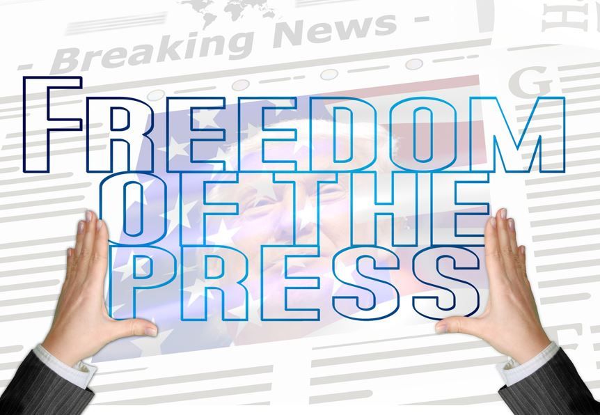 Freedom of the Press - Schriftzug gehalten von links und rechts durch Hände. Hintergrund Tageszeitung