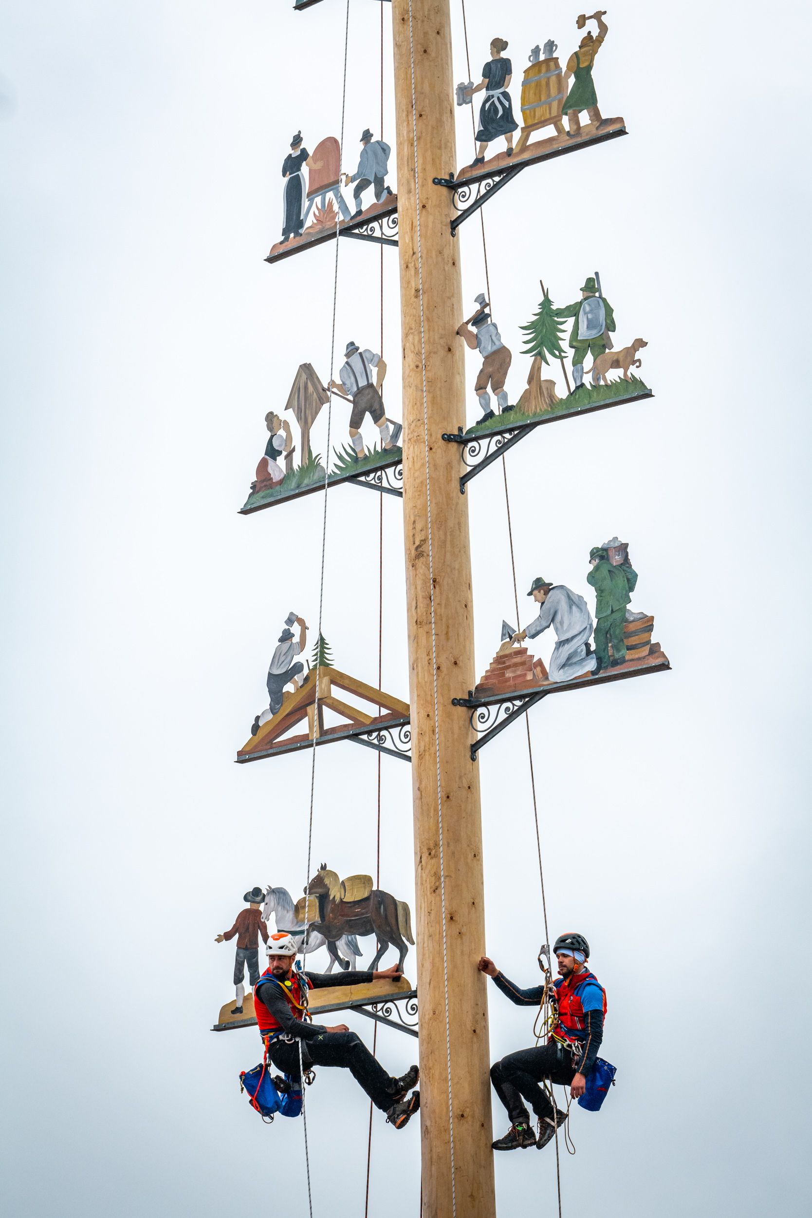 Zwei Bergwachtler hängen mit Seilen gesichert hoch oben bei den Motivtafeln am Maibaum Grainbach