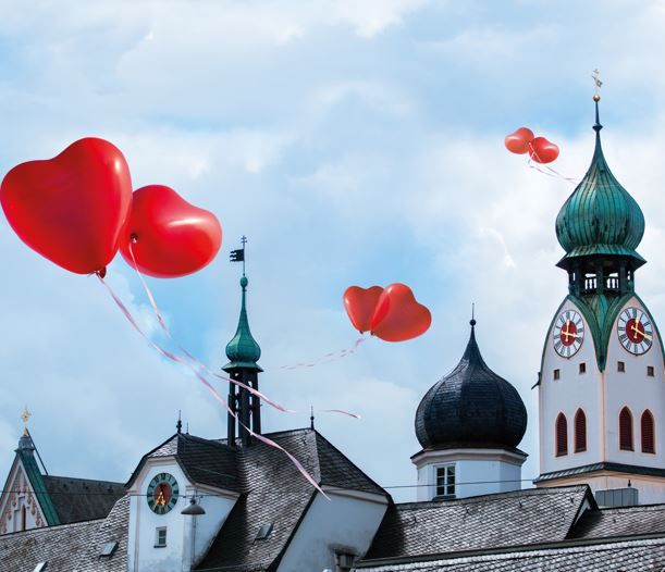 Blick auf Kirchturm St. Nikolaus und Dach von Mittertor. In der Luft schweben rote Herzballons