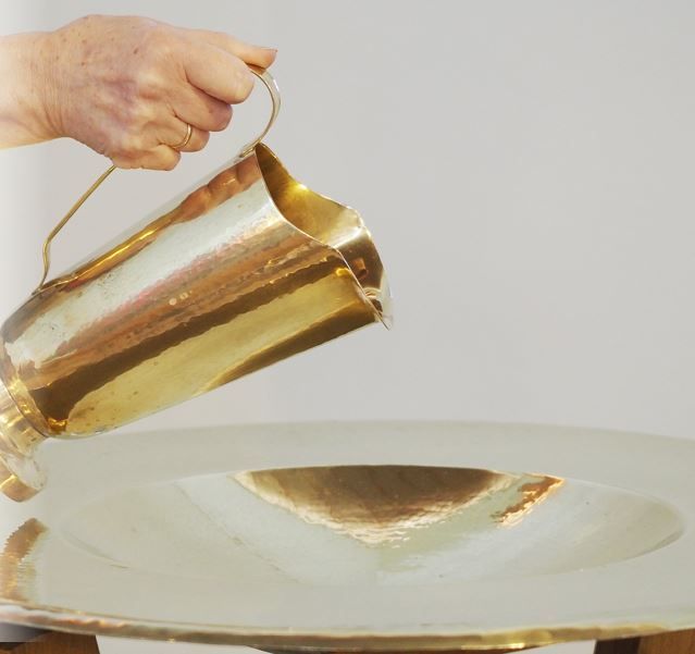 Aus foldfarbigem Kelch wird Wasser in eine goldfarbige Schüssel gegossen