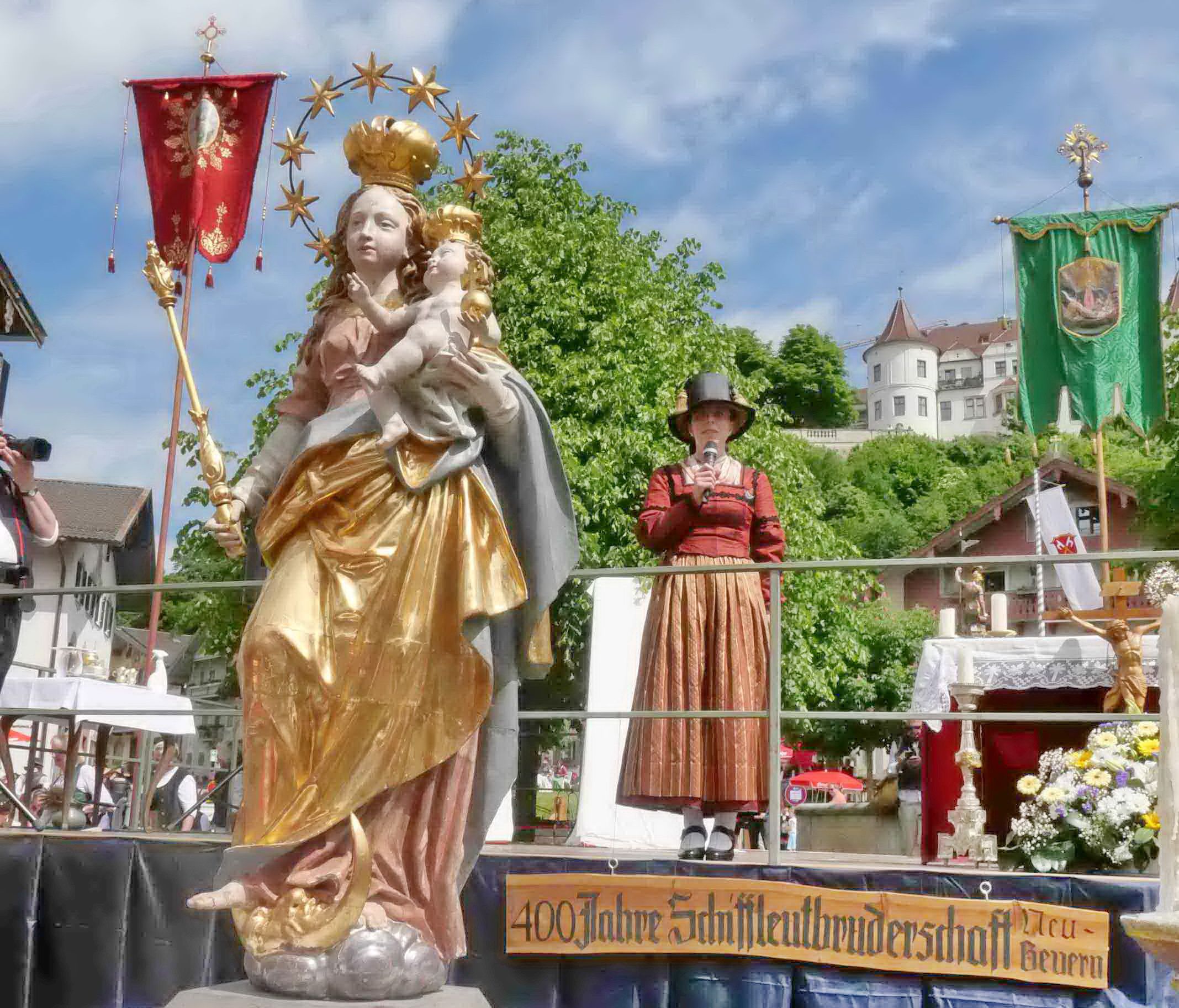 Maria-Statue Dahinter Frau in Tracht auf Bühne, dahinter auf Anhöhe Schloss Neubeuern