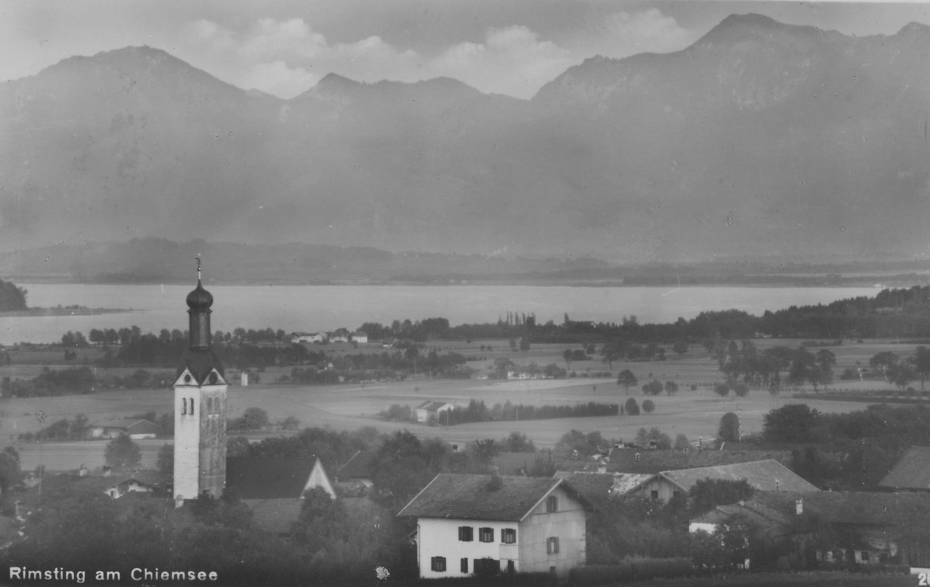 Schwarz-Weiss-Luftaufnahme von Rimsting mit Chiemsee und Bergen im Hintergrund