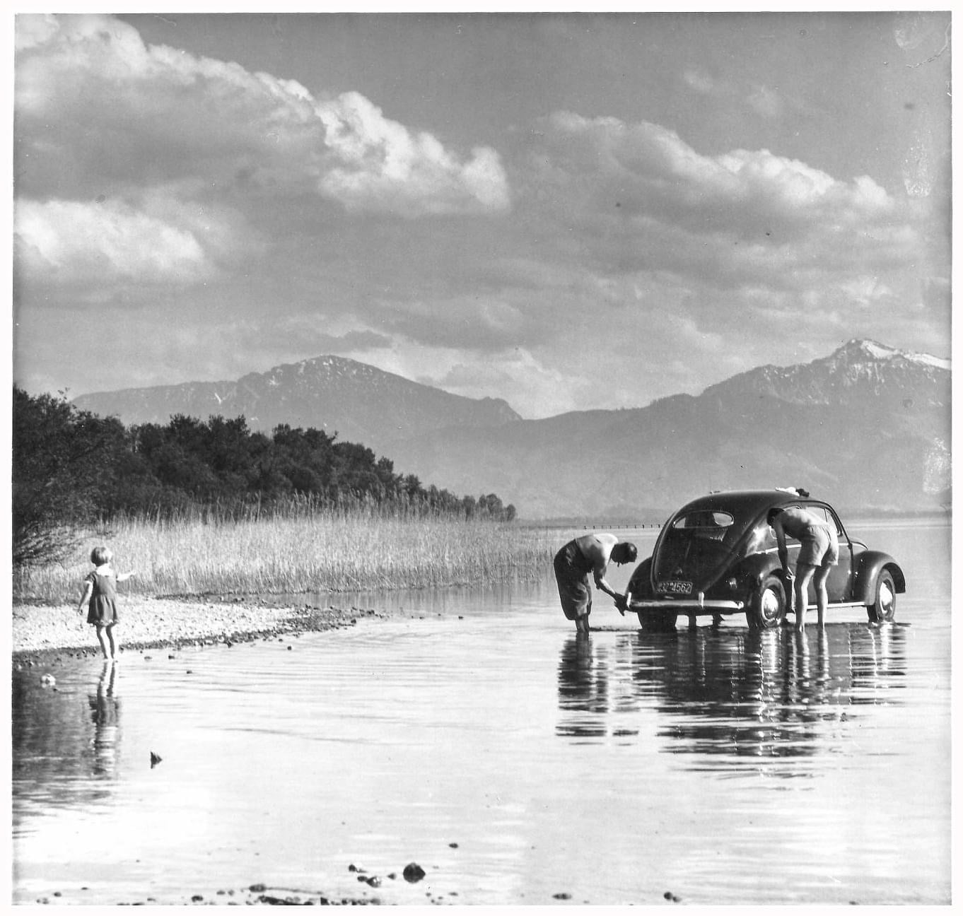 Foto aus dem Jahr 1957: Zwei Maenner waschen am Ufer des Chiemssee ihrenVW-Kaefer