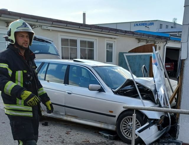Unfall Traunstein. Feuerwehrmann steht vor Auto, dass gegen eine Hauswand gefahren ist.
