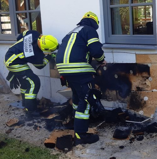 Zwei Feuerwehrmaenner oeffnen Hausfassade, um an Glutnester zu kommen