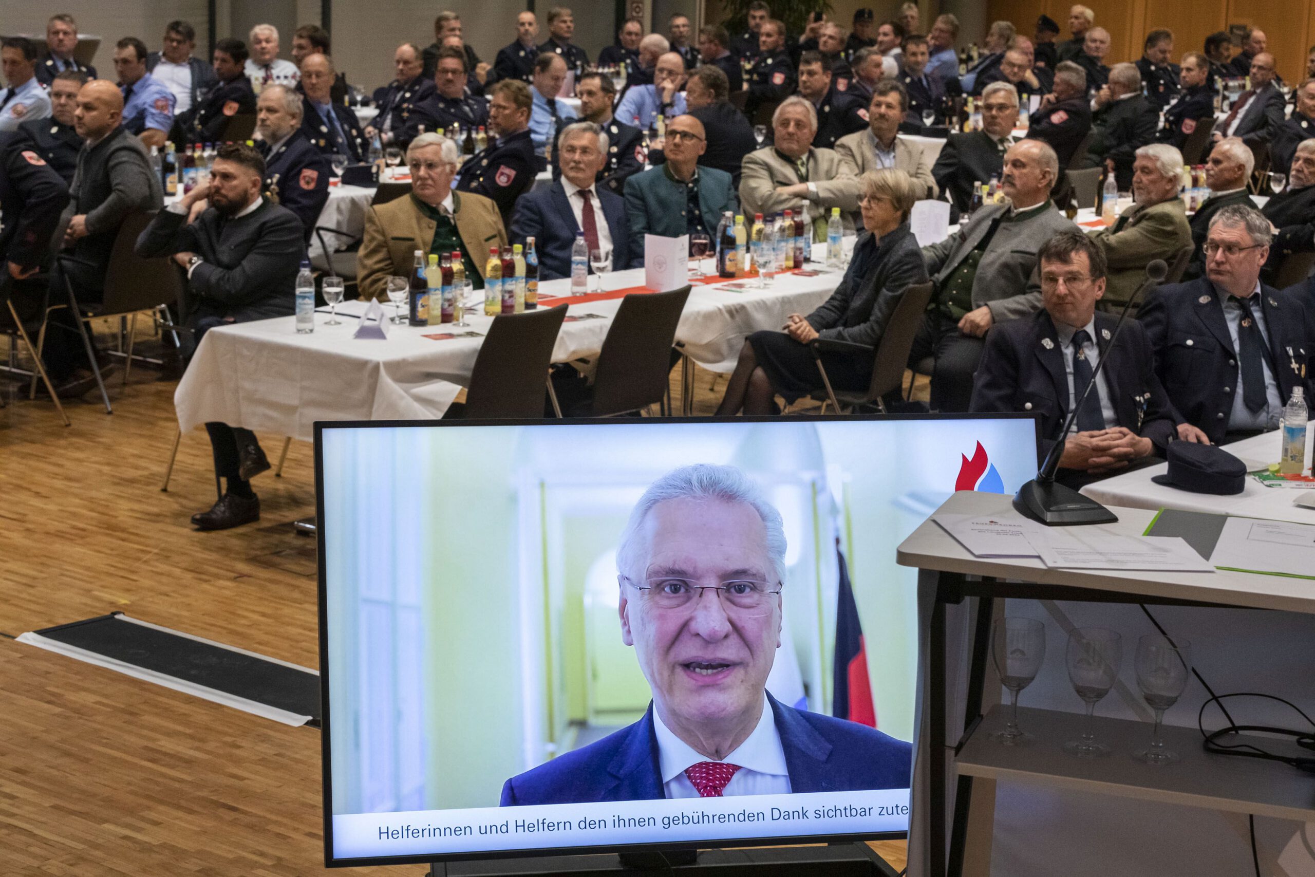 Kreisfeuerwehrverband Traunstein - Ehrung, Blick in den Saal, im Vordergrund Bildschirm. darauf zu sehen der Bayerische Innenminister Joachim Herrmann