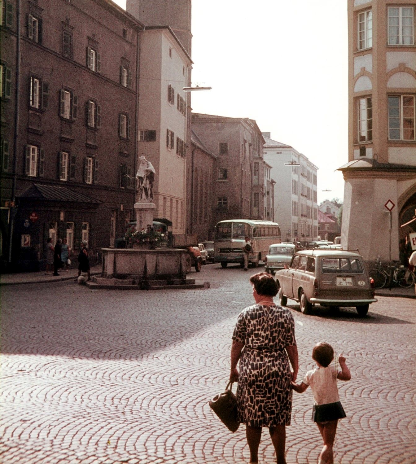 Blick auf den Max-Josefs-Platz vor dem Nepomukbrunnen im Jahr 1967. Im Vordergrund von hinten eine Mutter mit ihrem kleinen Kind