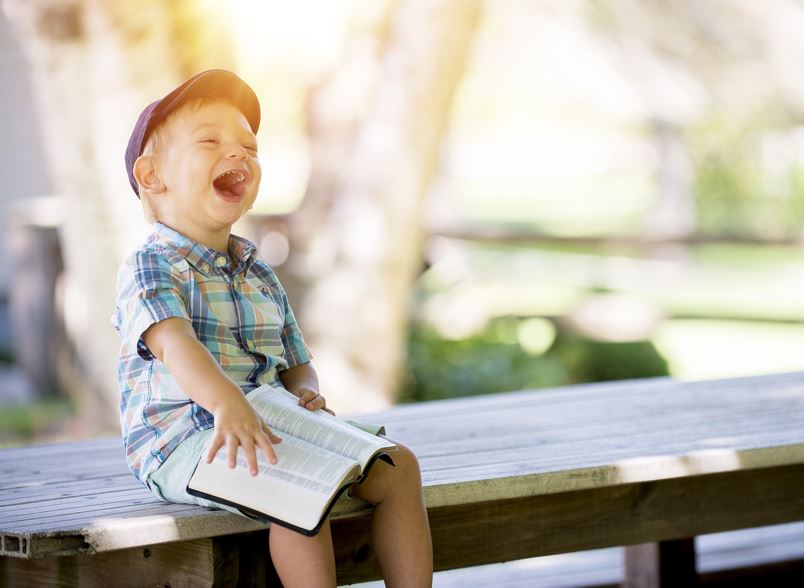 Kleiner Junge hält aufgeschlagenes Buch auf dem Schoss und lacht