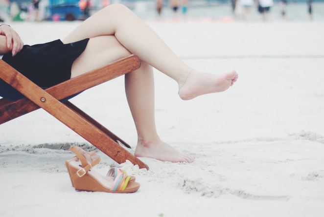 Frau auf Liegestuhl am Strand. Zu sehen nur ihre Beine