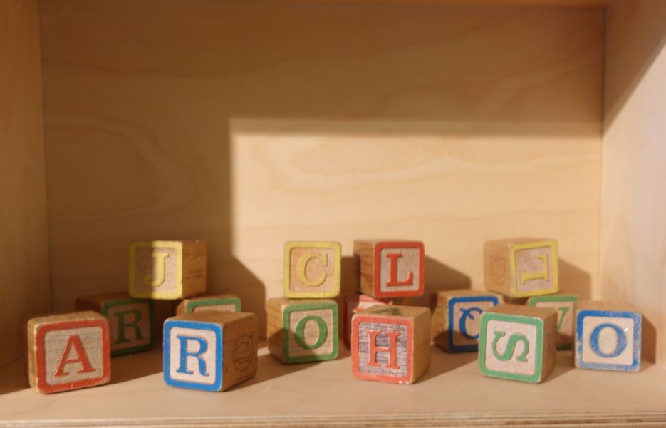kleine, bunte Holzkloetze mit Buchstaben in einem Holzregal