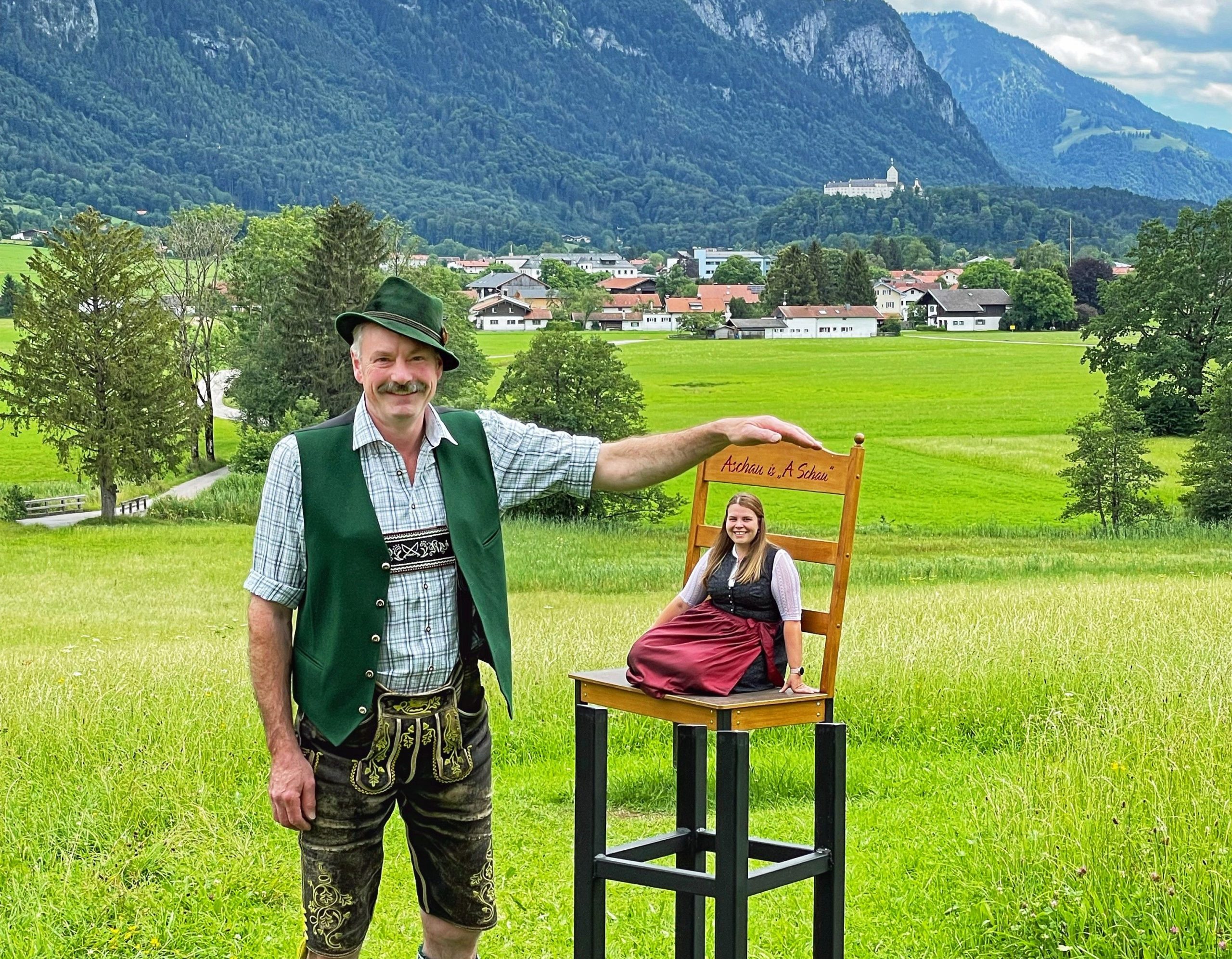 Beulet Stuhl in Aschau im Chiemgau. Optische Taeuschung laesst Mann neben Stuhl wie einen Riesen wirken und Frau auf Stuhl wie einen Zwerg