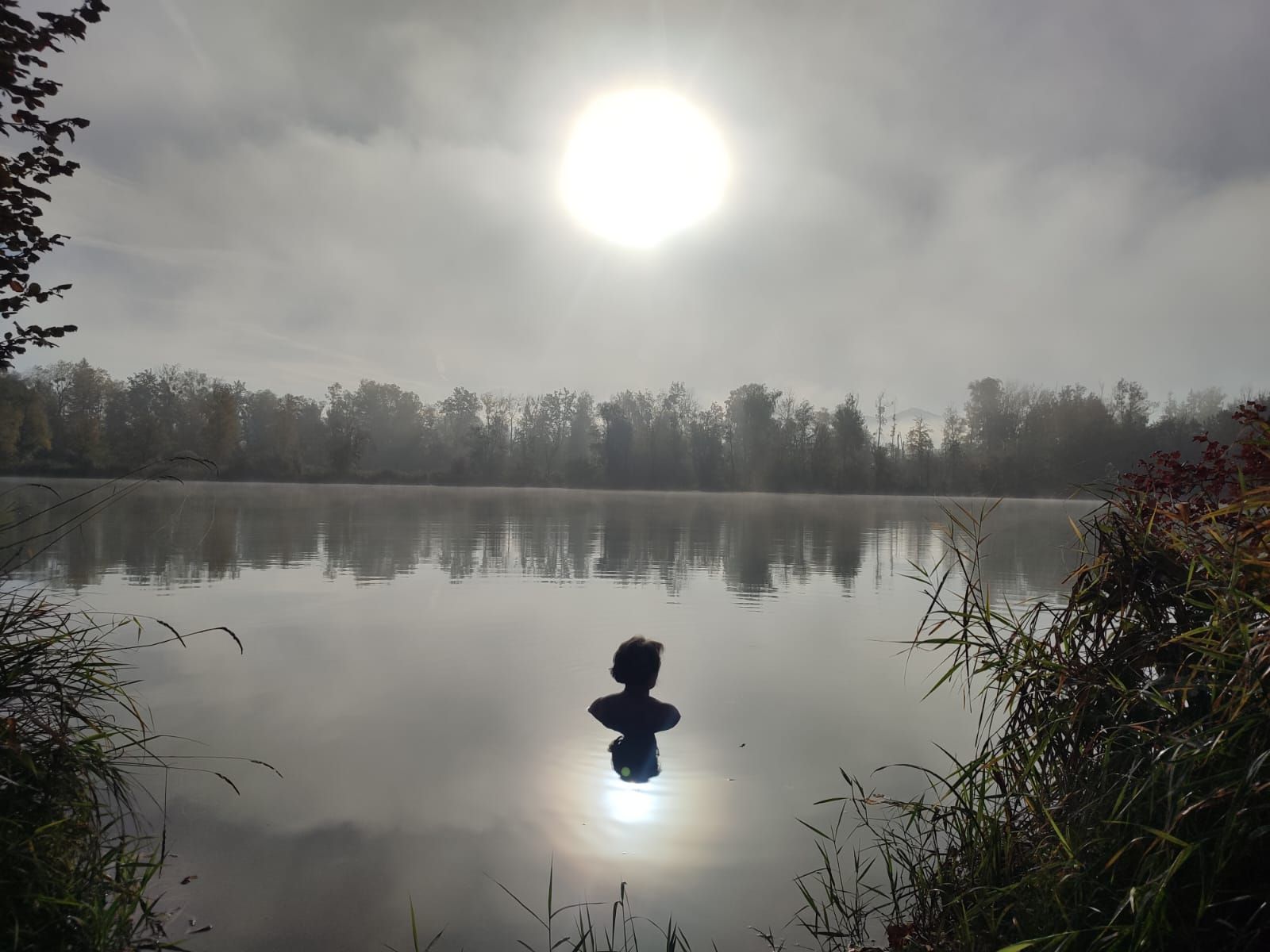 Schatten von Frau, die bei Nebel mit Vollmond am frühen Himmel im Happinger See in Rsoenheim schwimmt