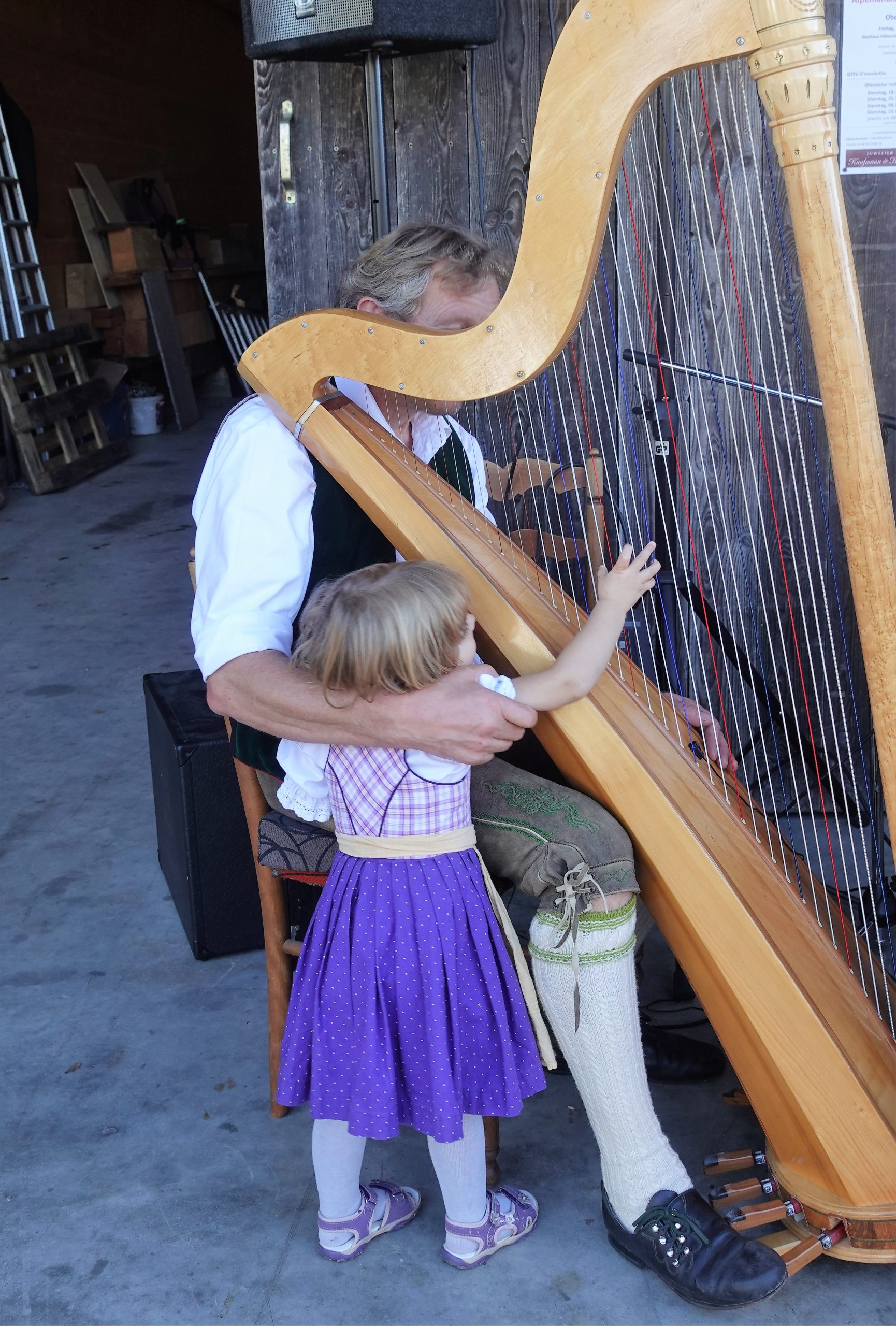Kleines Kind in lila Dirndl zupft an der Harfe