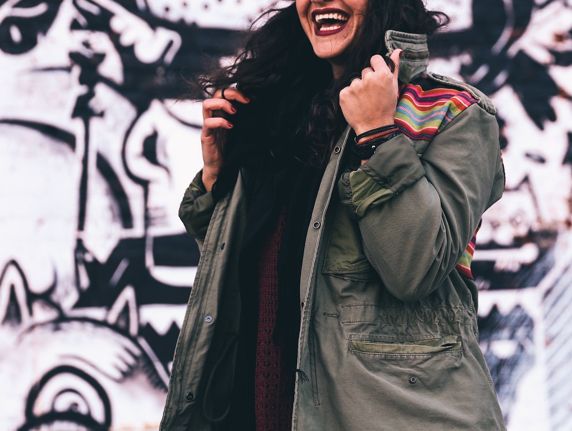 Frau mit Mantel lachend vor Graffiti-Wand