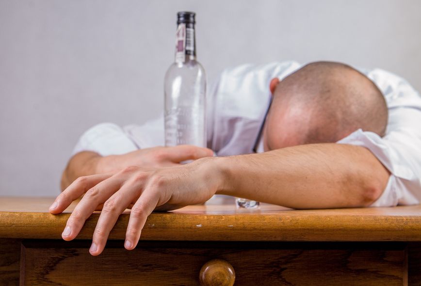 Betrunkener Mann mit Glatze liegt mit Flasche in der Hand auf dem Tisch