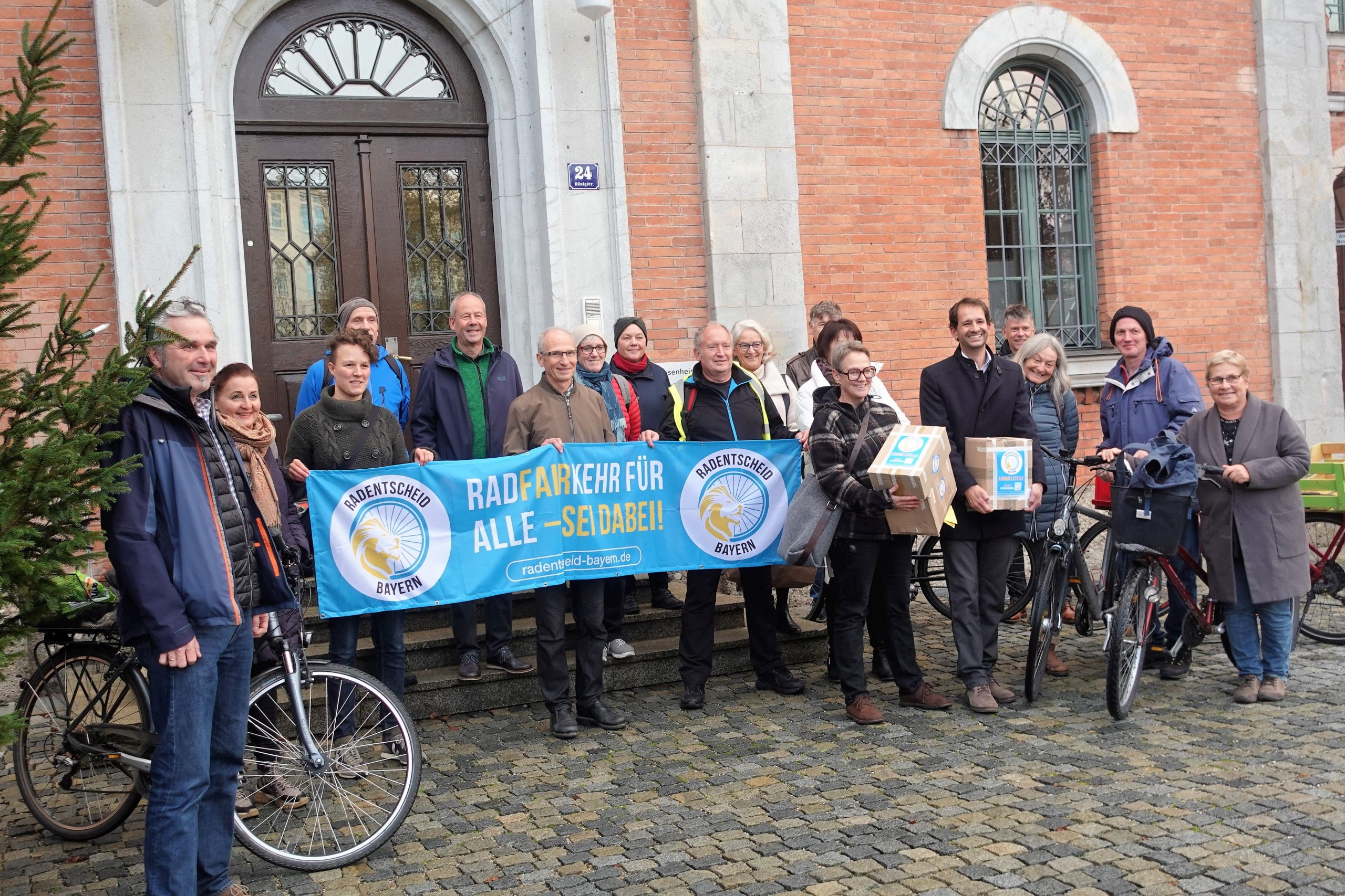 Menschen mit Plakat, Unterschriftenpaketen und einem Fahrrad vor dem Rathaus Rosenheim