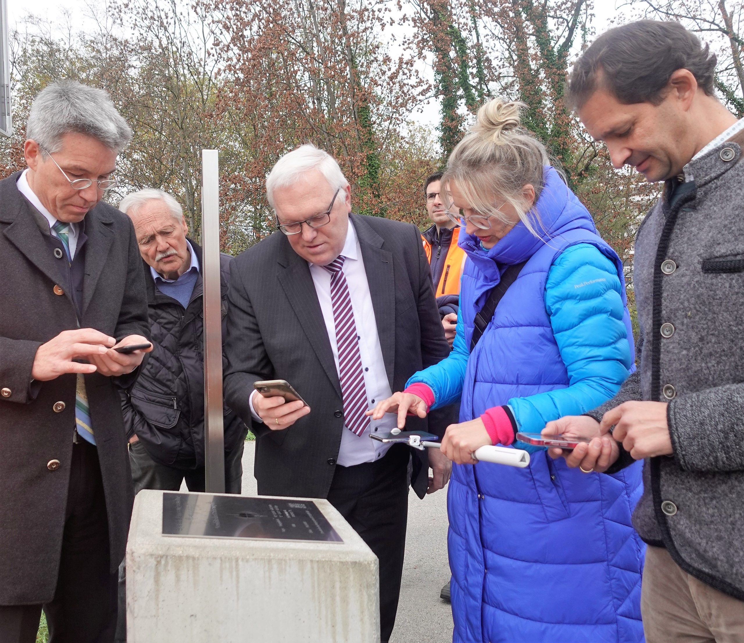 Fünf Personen probieren mit ihrem Handy den Geodätischen Referenzpunkt im Mangfallpark in Rosenheim aus