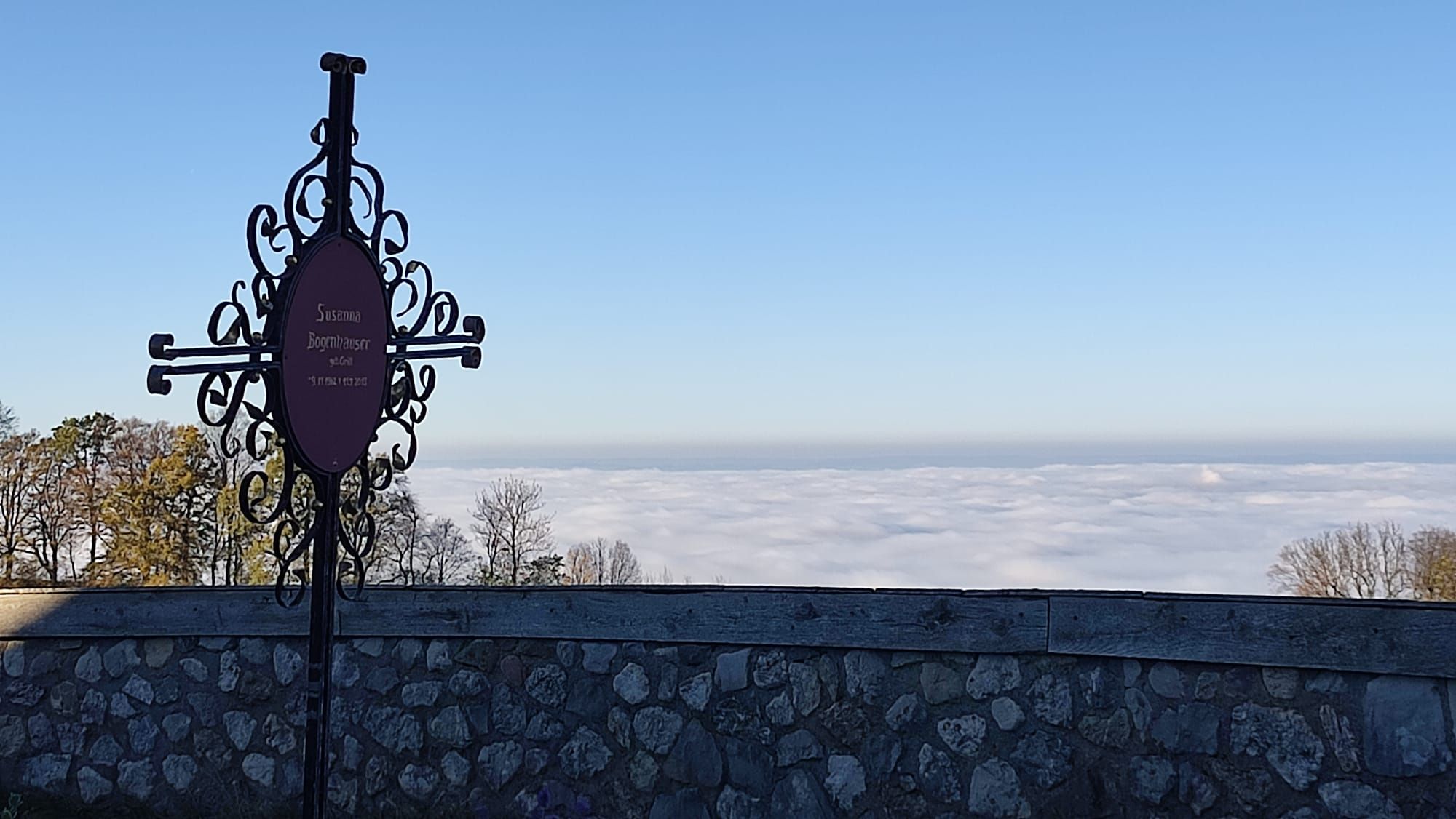 Blick über Friedhofsmauer mit Schmiedekreuz hin zu dickem Nebel