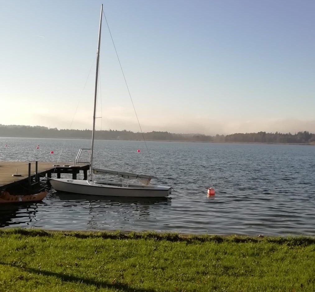 Blick auf den Simssee in Landkreis Rosenheim mit vorne Wiese, Steg und Segelboot an der Boje