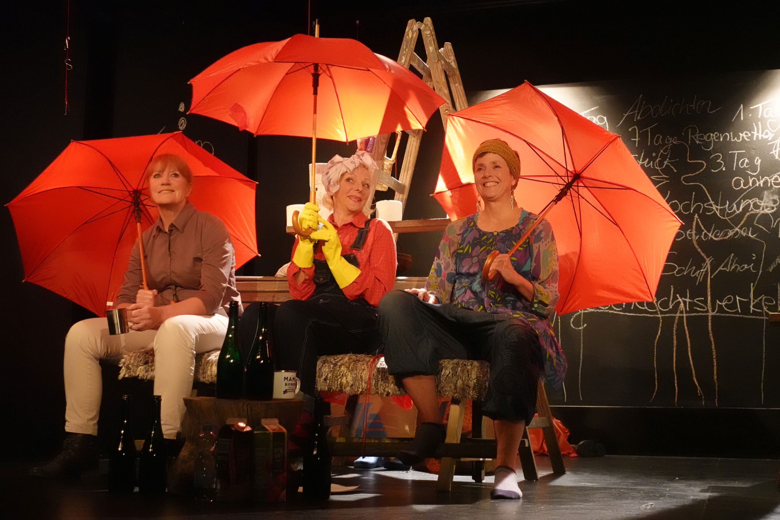 Die drei Schwestern auf der Bühne mit roten Regenschirmen