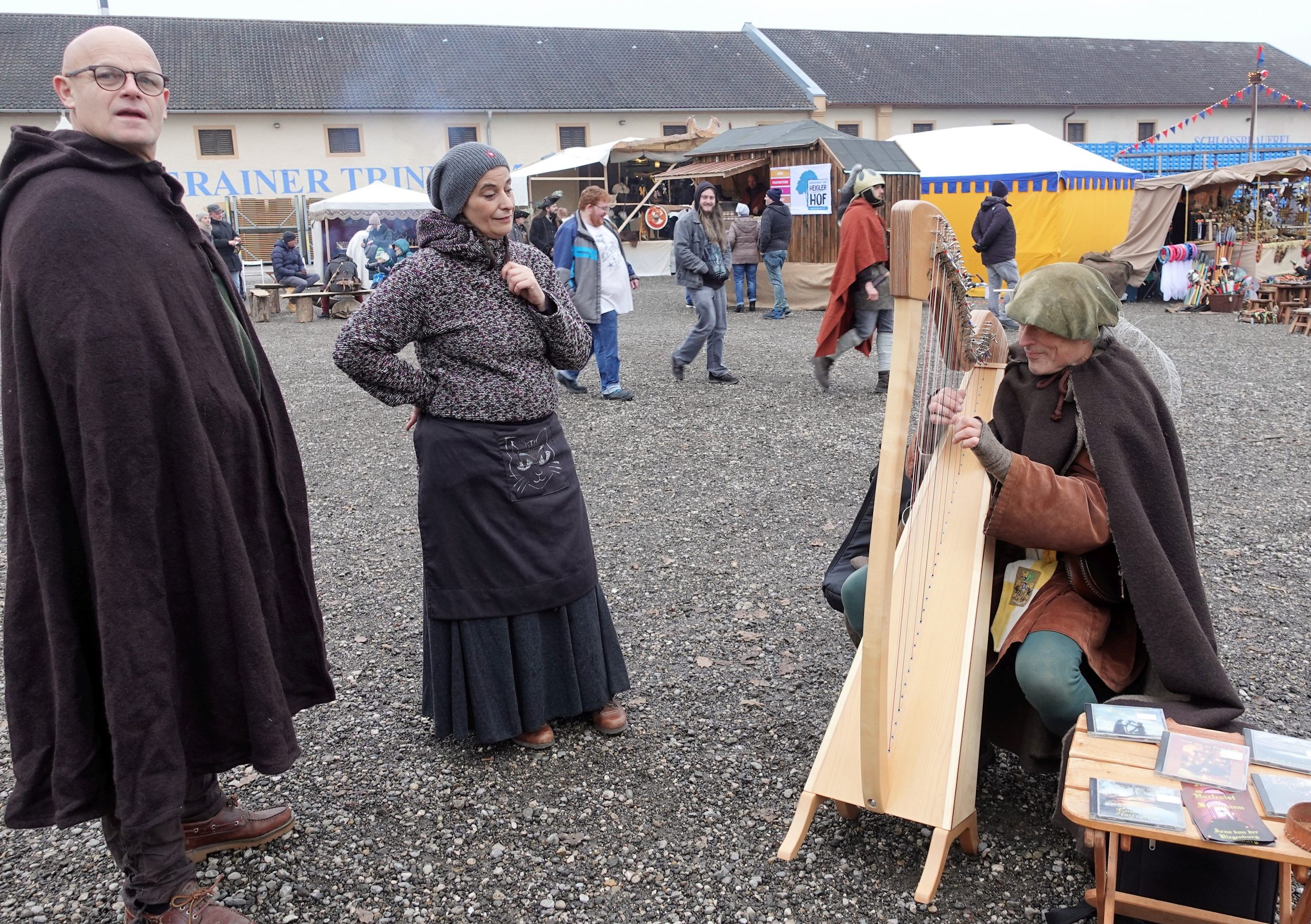 zwei mittelalterlich gekleidete Besucher lauschen einem mittelalterlichem Harfenspieler