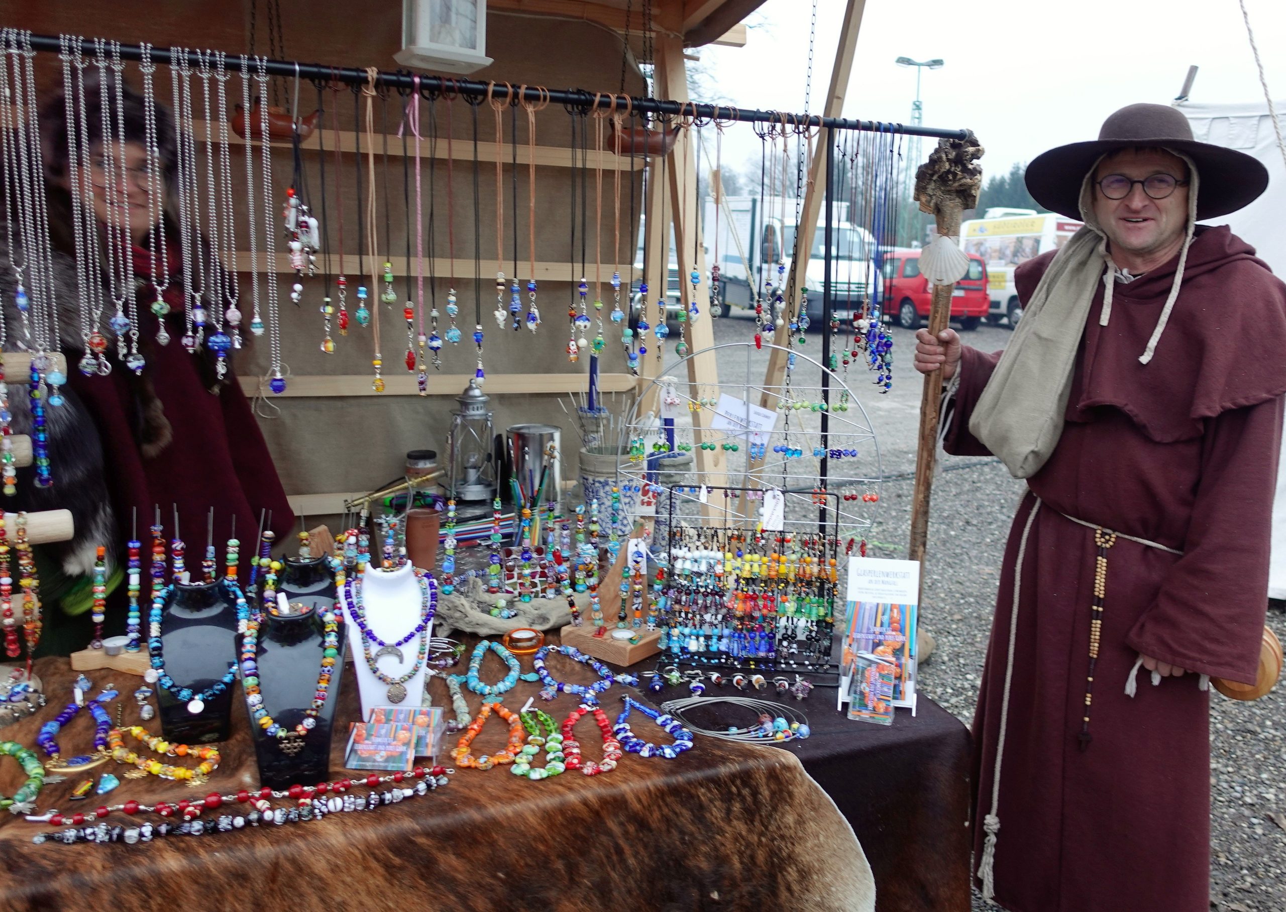 Ein mittelaltelterlich verkleideter Verkäufer neben einem Stand mit Glasperlen