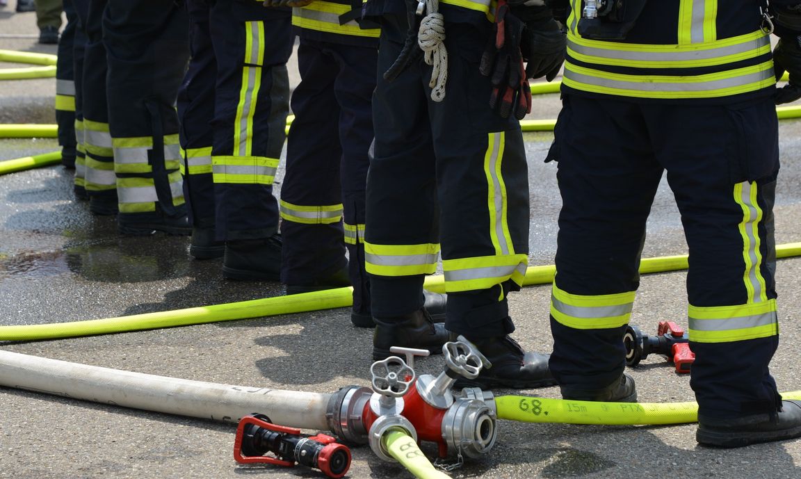 Blick auf die Beine von Feuerwehrmännern mit Löschschlauch am Boden