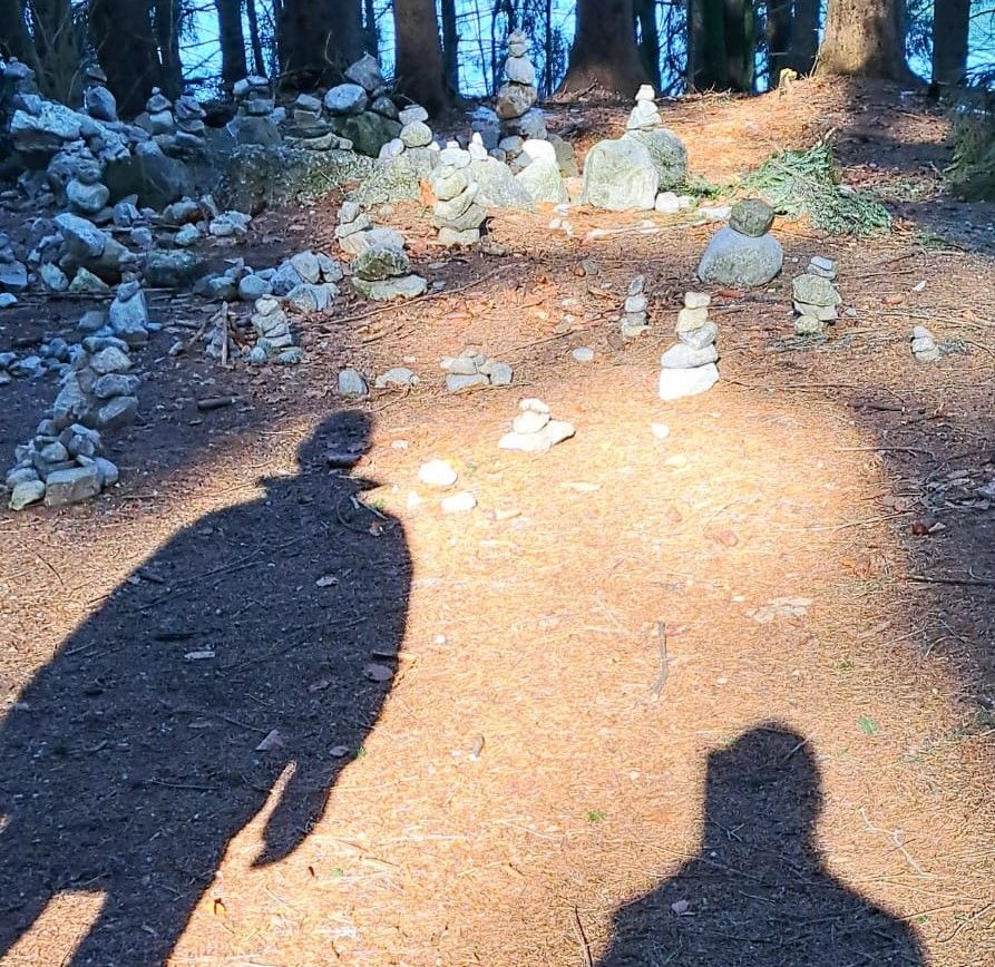 Schatten von zwei Wanderern und oben am Bild aufeinander gestapelte Steine
