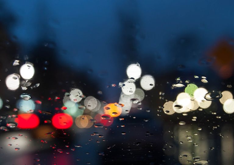 Blick auf Lichter in der Stadt bei Dunkelheit durch eine Windschutzscheibe mit Regentropfen
