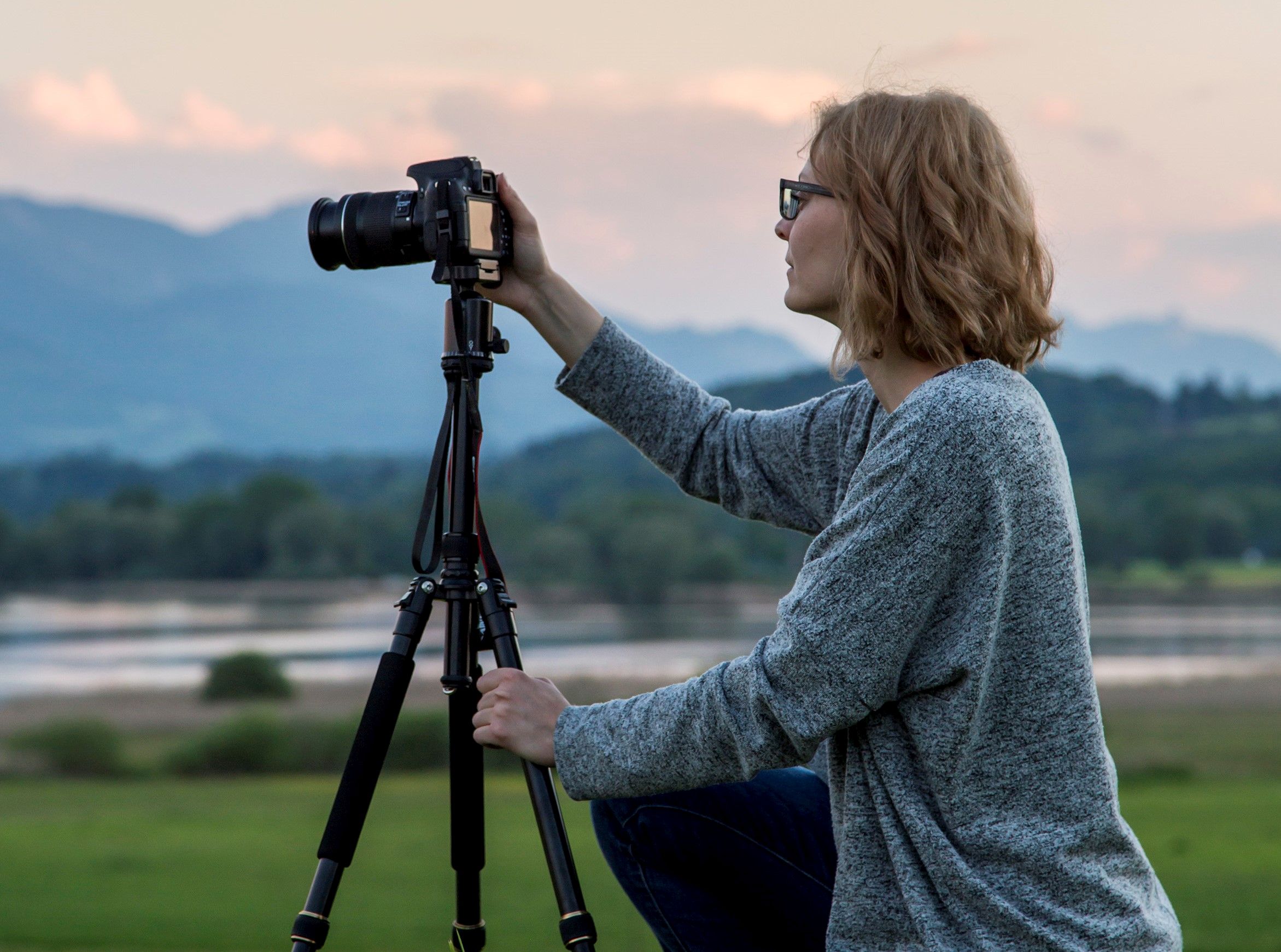 Fotografin knie im Gras und fotografiert mit Kamera auf Stativ die Bergwelt in Prien am Chiemsee