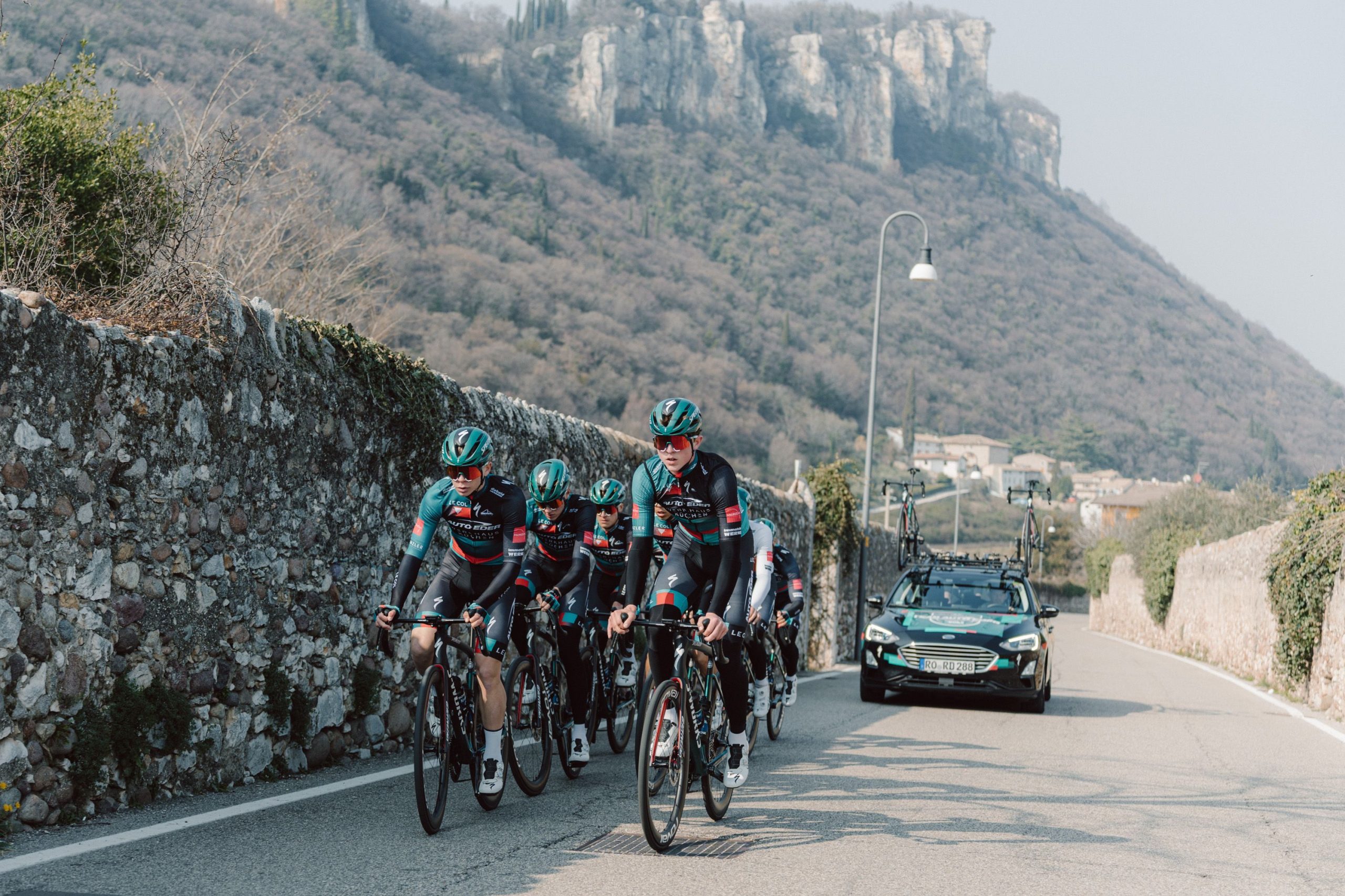 Rennradsportler des Team Auto Eder radeln gefolgt von einem Teamauto einen Berg am Gardasee hoch