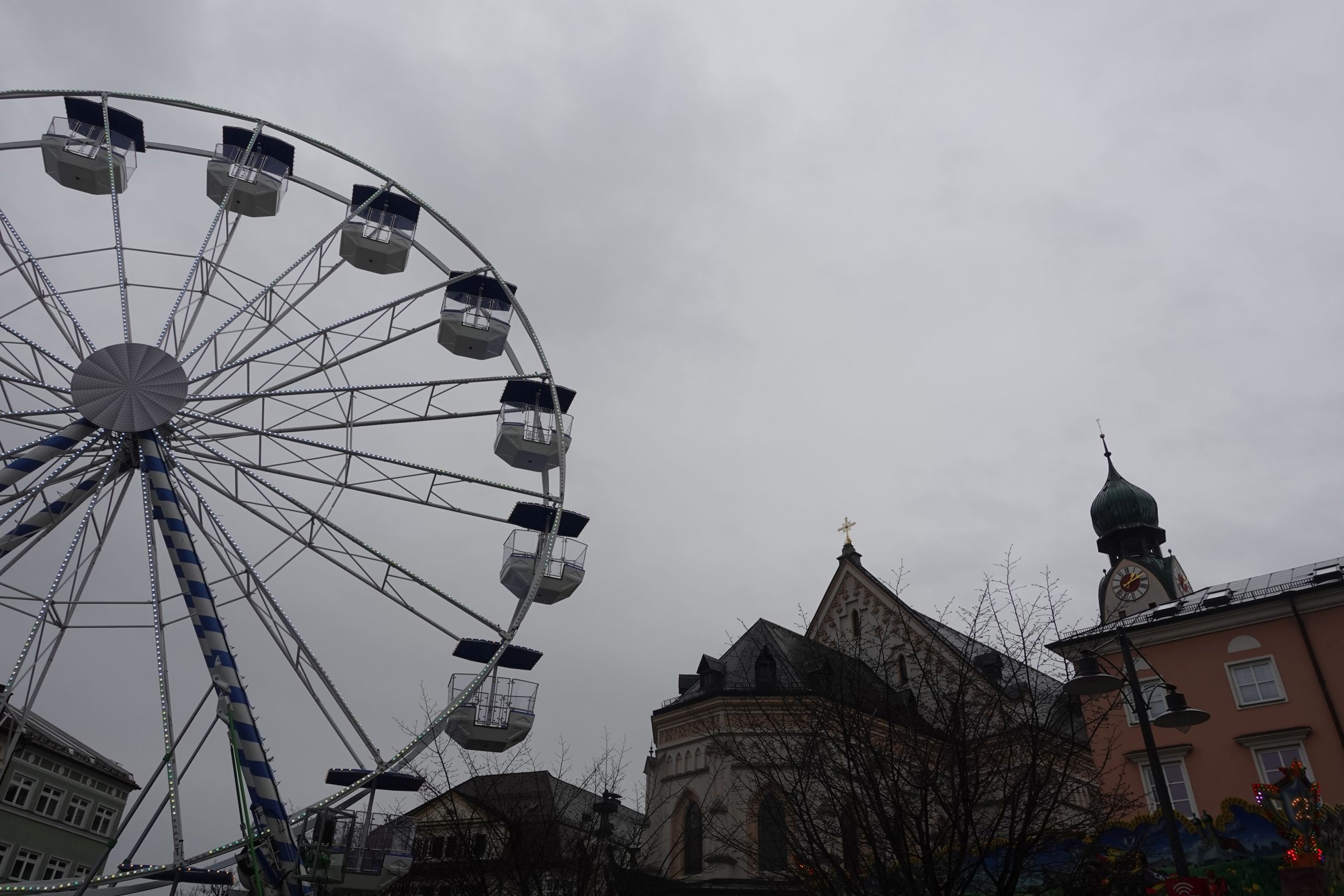 Blick hinauf zum Riesenrad am Ludwigsplatz in Rosenheim. Daneben Kirchturm von St. Nikolaus im Hintergrund. Himmel bedeckt