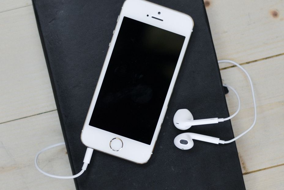 Handy und Kopfhörer Apple auf schwarzem Brett auf hellen Holztisch
