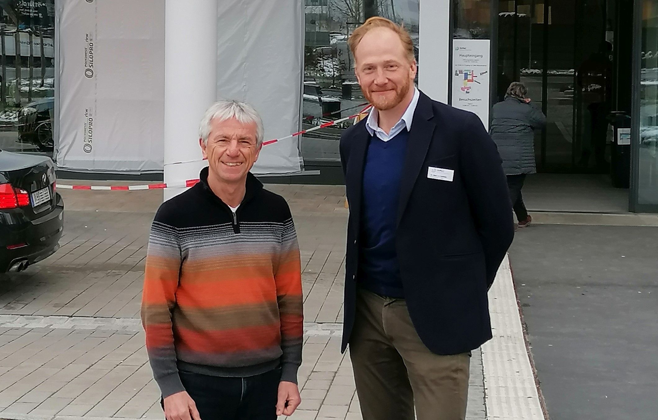 Der neue Patientenfürsprecher der RoMed Kliniken Rosenheim Volker Schmidt links und der Kaufmännische Leiter Dr. Max von Holleben rechts vor dem Eingang des Krankenhaus in Rosenheim