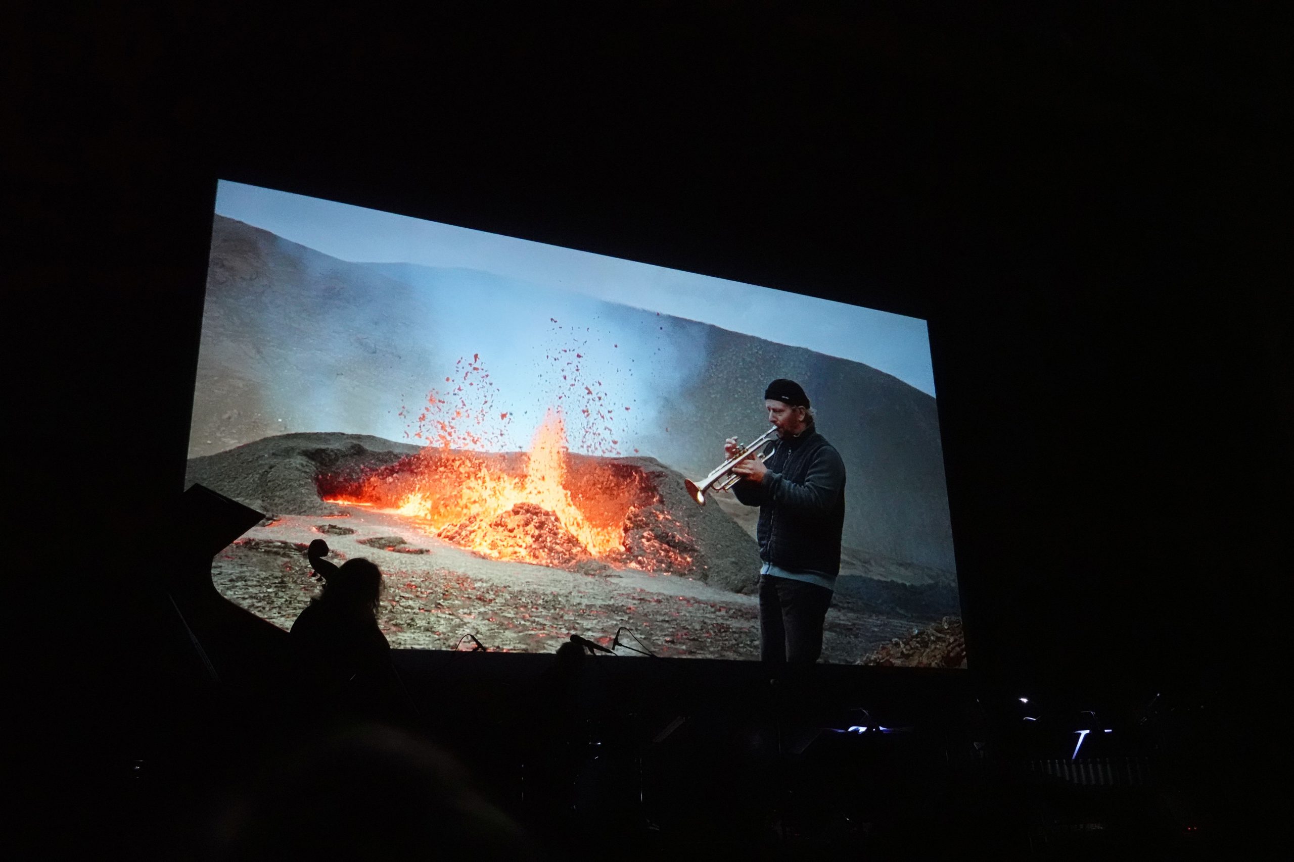 Blick zur Leinwand, wo Musiker vor einem brodelnden Vulkankrater spielt