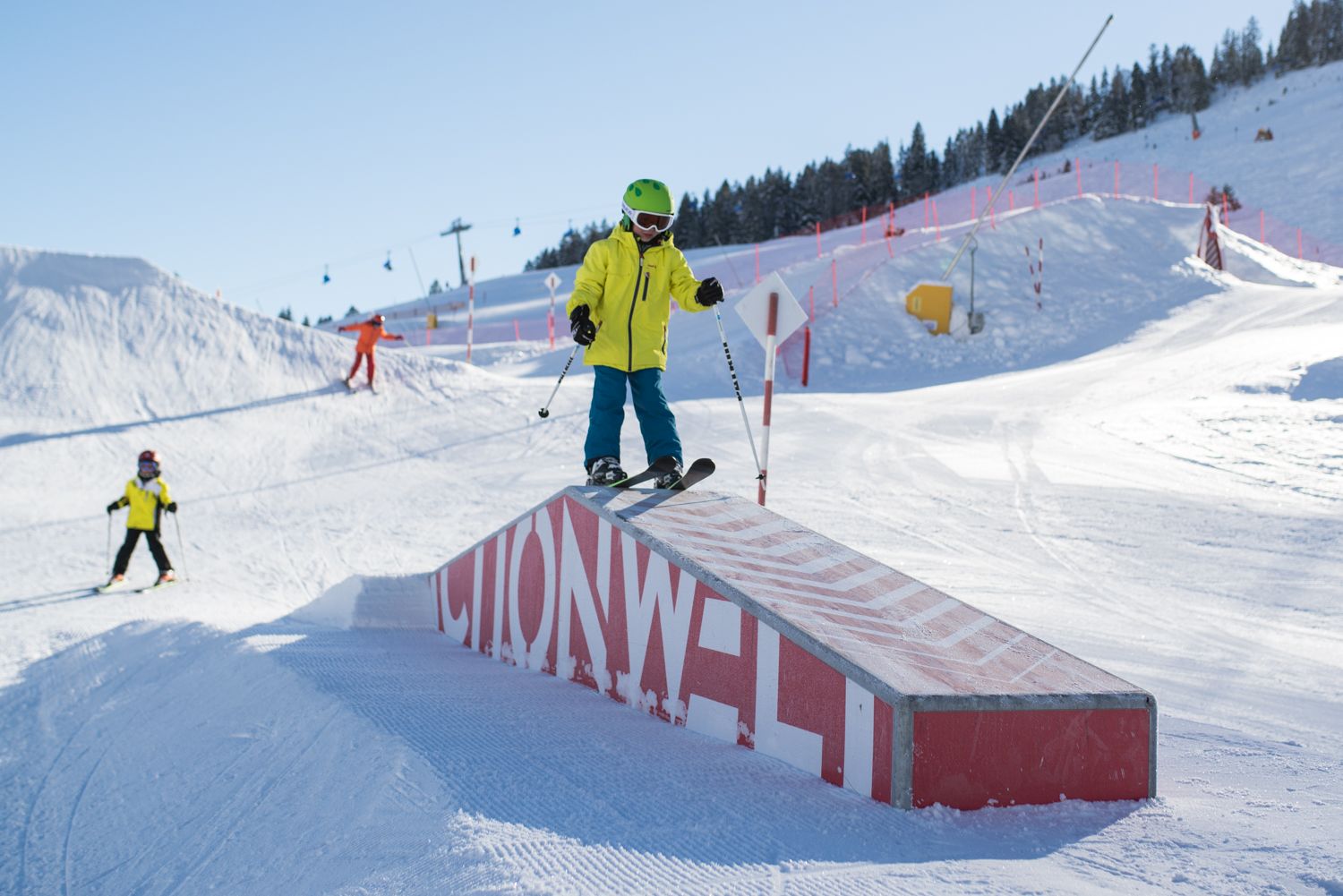 Kleiner Skifahrer mit neongelber Skijacke steht auf einer Rampe